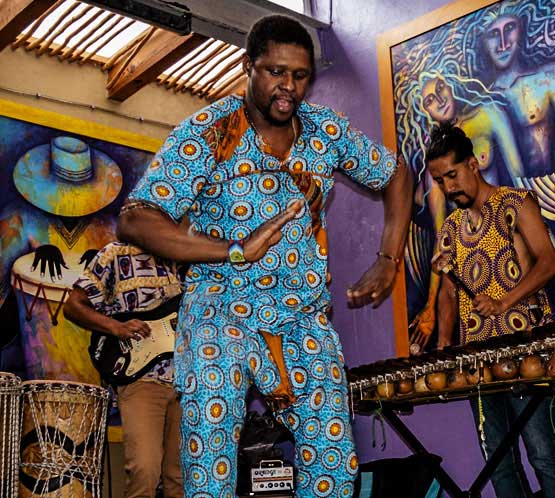 Percusionista con camisa azul sostiene un tambor junto a otros músicos.